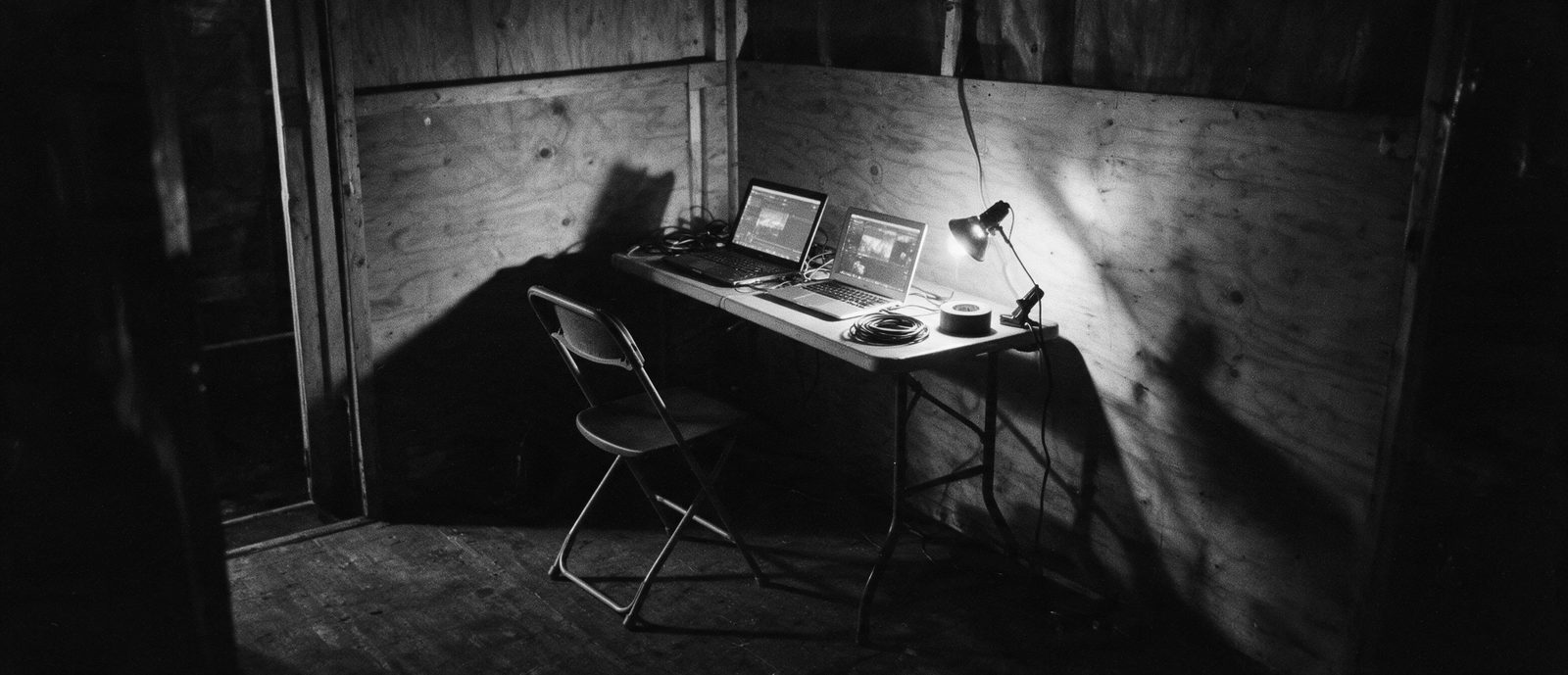 A production cabin behind a stage at four in the morning: a folding table, two open laptops, coiled cables, an empty chair.